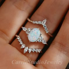 a woman's hand holding three rings with white opal and diamonds on them