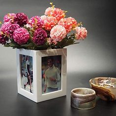 a vase with flowers in it next to a photo frame and two bowls on the table