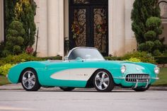 a turquoise and white classic car parked in front of a large building with columns on it