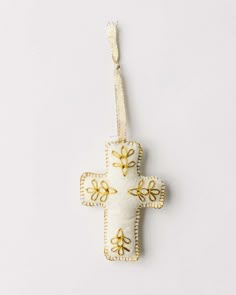 a white cross ornament hanging from a string on a wall with gold accents