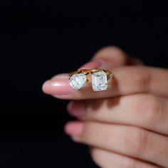 a woman's hand holding an engagement ring with two stones on it and the other side