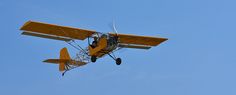 a small yellow airplane flying through a blue sky