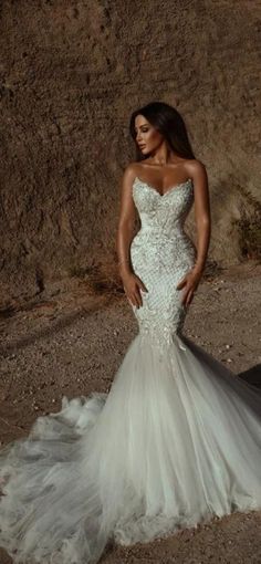 a woman in a white wedding dress standing on the side of a mountain with her hands on her hips