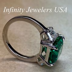 "-Approximate total carat weight: approx. 6.00ctw diamond equivalent #7080 -Center Stone Size: 11x9mm - approx. 4.90ct diamond equivalent -Center Stone Shape: emerald cut -Gem Type: lab created Green Emerald -Stone Clarity: VS2 -Stone Color: F -Moh's Scale: 9 hardness -Side Stones Size: 6x4mm trapezoid approx. 0.55ct. each diamond equivalent -Gem Type: Zonar moissanite -Metal Type and Purity: 14k white gold -Setting: 4 prong tulip setting -Stock Ring Size: 5.75 -Country of Manufacturing: USA (Mi 14k Gold Green Diamond Princess Cut Ring, Princess Cut Green Diamond Ring In 14k Gold, Green Princess Cut Diamond Ring In 14k Gold, Gia Certified Trillion Cut Emerald Wedding Ring, Green Diamond Ring With Princess Cut And Accent Stones, Green Princess Cut Diamond Ring With Accent Stones, Luxury Green Heart Cut Rings, Green Diamond Ring In 14k Gold For Anniversary, Green Emerald Ring With Brilliant Cut For Promise