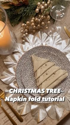 a christmas tree napkin on top of a plate next to a candle and some silverware