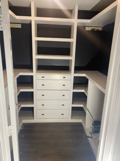 an empty walk in closet with white drawers and black shelves on both sides, along with dark wood flooring