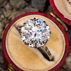 a diamond ring sitting on top of a red velvet box next to other jewelry items