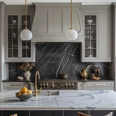 a kitchen with marble counter tops and gold accents on the cabinets, along with two hanging lights