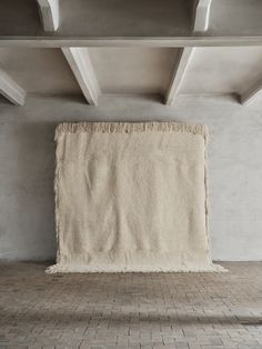 an empty room with a large rug hanging from the ceiling and brick flooring in front of it