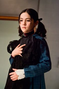 a woman is dressed in black and holding her hands on her chest while standing next to a wall