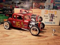 a red toy car sitting on top of a wooden table next to other toy cars