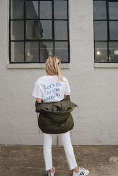 a woman standing in front of two windows wearing a t - shirt that says let's go to the studio