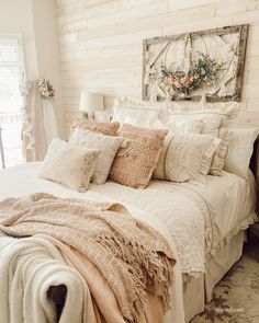 a white bed topped with lots of pillows next to a wooden headboard covered in blankets