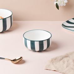 two black and white striped bowls with gold spoons next to each other on a pink surface