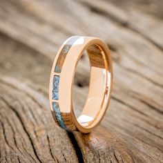 a gold wedding ring with blue opal inlays on top of wooden plank