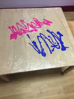 a wooden table covered in plastic wrap with graffiti writing on the top and bottom side