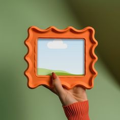 a hand holding an orange frame with a sky and clouds on it