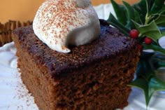 a piece of chocolate cake on a white plate with holly leaves and berries in the background