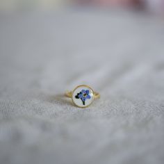 A simple ring to add a touch of nature to any outfit! This ring is handmade using pressed Forget Me Not flowers preserved in resin, and the ring is Sterling Silver. The Forget Me Not flower has so many meanings, and makes a great gift or stocking filler to someone you care about. It's best to not wear this ring in the shower/bath etc, and every time you wash your hands, as it's handmade, but every once in a while should be fine. Delicate Promise Rings With Birth Flower, Adjustable Flower Enamel Ring As Gift, Delicate Birth Flower Jewelry Ring, Dainty Birth Flower Ring Jewelry, Dainty Promise Flower Ring With Birth Flower, Promise Ring With Birth Flower Detail, Dainty Enamel Ring For Gift, Dainty Enamel Ring As A Gift, Dainty Enamel Round Ring As Gift