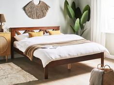 a bed with white sheets and pillows in a bedroom next to a plant on the wall