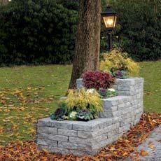 a brick planter with flowers in it next to a tree