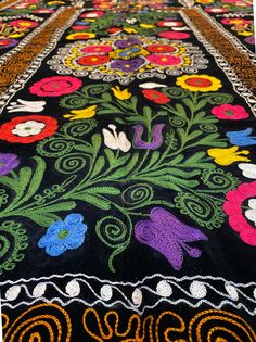 an embroidered table runner with flowers and swirls on black ground, in front of white background