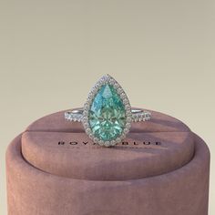 a fancy ring with an aqua blue diamond in the center on top of a pink velvet box