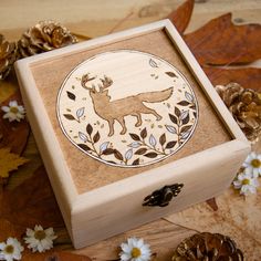 a wooden box with a deer design on the lid and flowers around it, surrounded by leaves