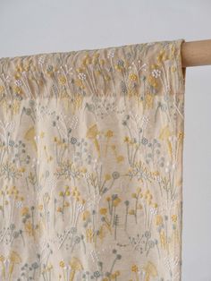 a curtain with yellow and blue flowers on it hanging from a wooden rodon over a window