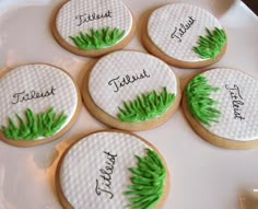 four decorated cookies on a white plate with green leaves and the word trust written on them