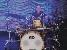 a man is playing drums on stage in front of a large screen with blue lights