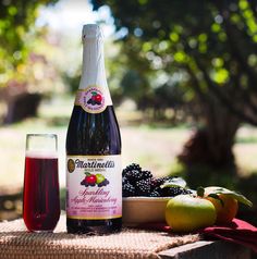 a bottle of wine sitting next to some fruit on a picnic table with apples and grapes