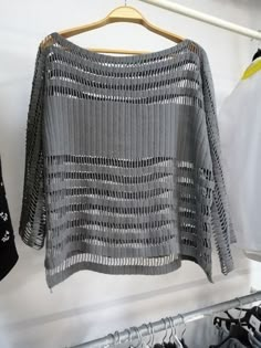 an open knit sweater hanging on a clothes hanger next to some shirts and jackets