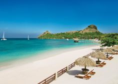 an empty beach with chairs and umbrellas on the sand next to the blue water