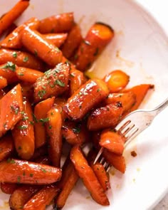 a white plate topped with carrots covered in sauce and seasoning next to a fork