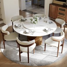 a round table with white chairs and plates on it in the middle of a room