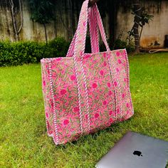 a pink bag sitting on the grass next to an apple laptop