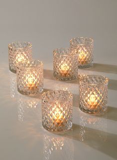 four glass tealight candles sitting next to each other on a white surface with reflections