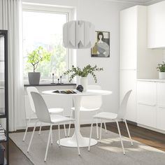 a white dining room table with four chairs and a plant in the corner next to it