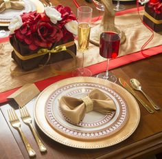 the table is set with gold and white plates, silverware, and red napkins