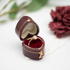 an open ring box sitting on top of a table next to a flower and a rose