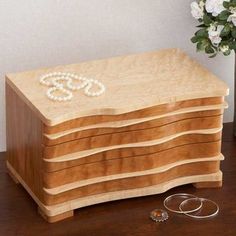 a wooden box with pearls on it sitting on a table next to two rings and a vase