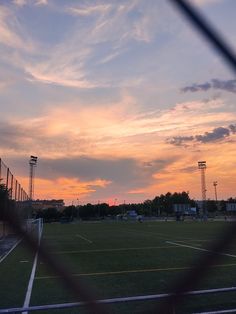 the sun is setting over a soccer field with lights in the distance and some clouds