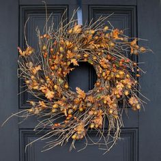 a wreath is hanging on the front door with autumn leaves and berries around it,