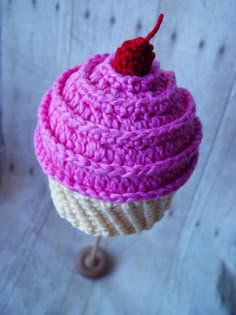 a pink crocheted cupcake with a cherry on top sitting on a stand