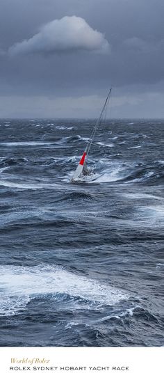 a sailboat in the middle of choppy ocean water with dark clouds overhead and red flag on it