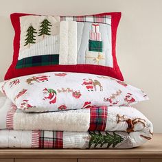 a stack of pillows and blankets sitting on top of a wooden dresser next to a christmas tree