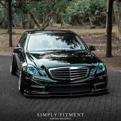 a green car parked on the side of a road in front of trees and bushes