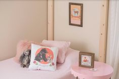 a pink bed with two stuffed animals on it and a small table in the corner