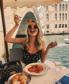 a woman eating spaghetti and drinking wine at an outdoor table with water in the background